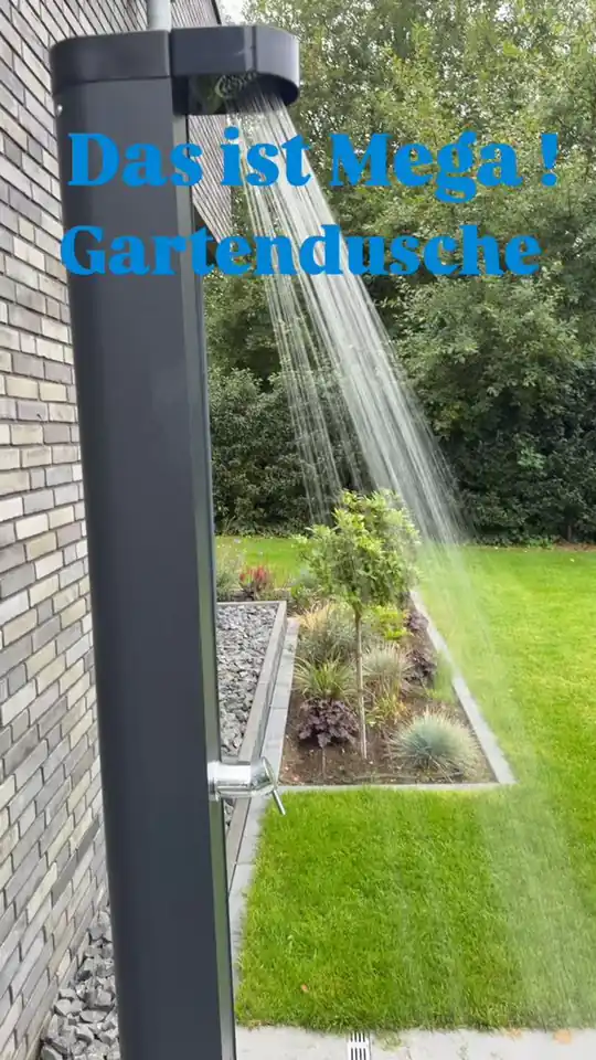 Gartendusche mit laufendem Wasser an der Hauswand neben Rasen und Beet
