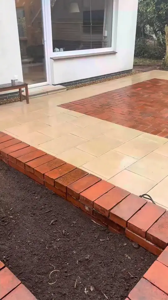 Neue Terrasse mit hellen Platten und rotem Klinkerband an der Hauswand