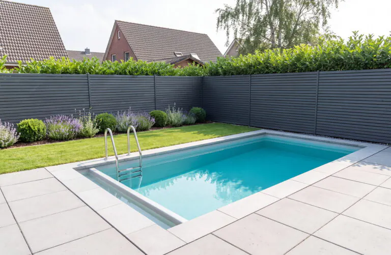Kleines rechteckiges Tauchbecken in einem schmalen Garten mit hellen Betonplatten, Edelstahlleiter, Lavendel und Sichtschutz aus anthrazitfarbenen Latten